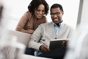 A couple, man and woman seated sharing a digital tablet.